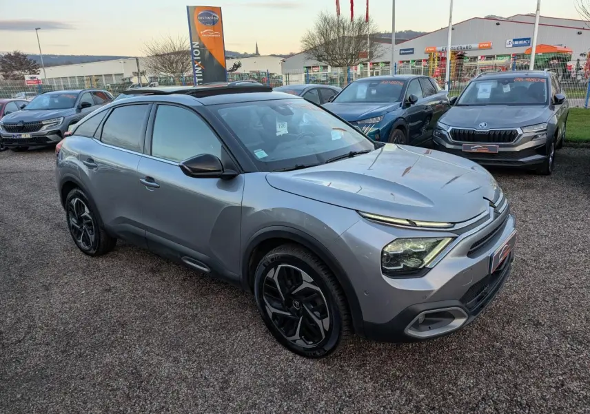 Citroën C4 gris métallisé vue 3/4 avant droit avec jantes alliage noires et toit ouvrant vitré.
