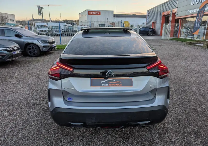 Vue arrière d'une Citroën C4 gris métallisé avec toit ouvrant vitré et feux arrière LED en V allumés.