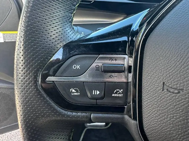 Gros plan sur les commandes multifonctions gauche du volant cuir perforé de la Peugeot 308 gris Artense 2022.