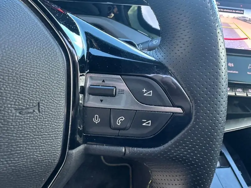 Gros plan sur les commandes multifonctions côté gauche du volant perforé noir de la Peugeot 308 Gris Artense.