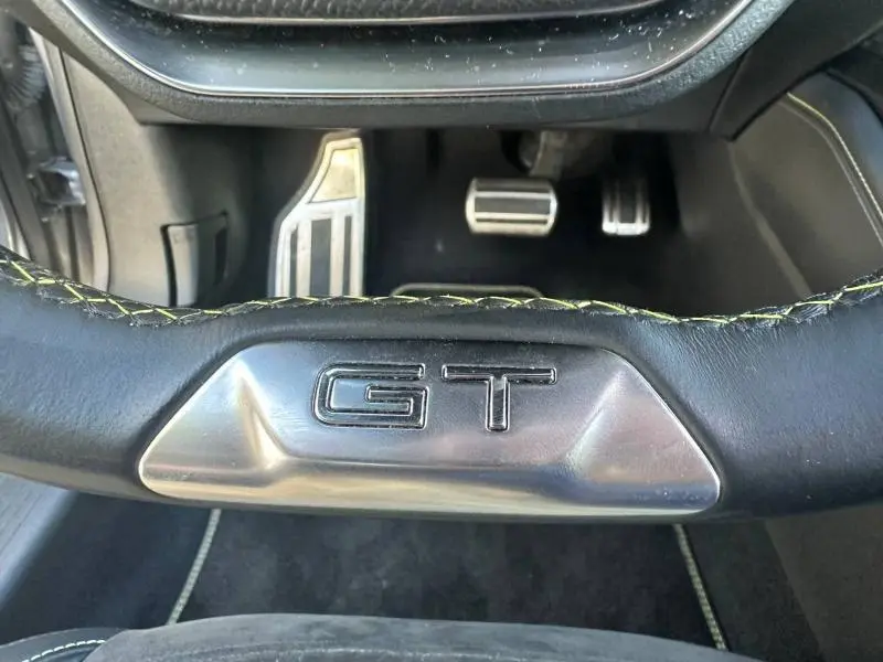 Gros plan sur le volant cuir noir avec logo GT et pédalier sport en aluminium dans une Peugeot 308 gris Artense.