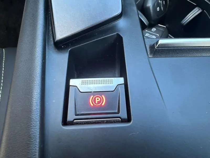 Gros plan sur le bouton de frein de stationnement électrique rouge dans la console centrale noire d'une Peugeot 308 Gris Artense.
