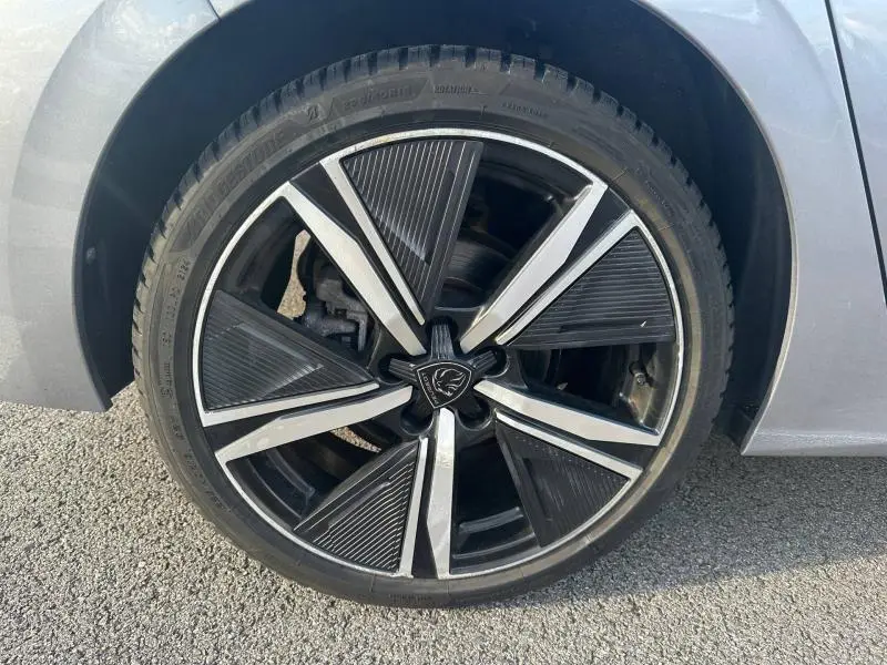 Gros plan sur la jante alu noire et argentée d'une Peugeot 308 gris Artense, avec logo lion au centre.