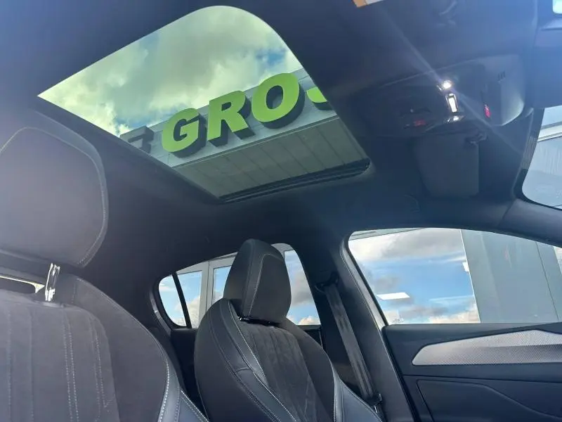 Vue intérieure avant droite du Peugeot 308 gris Artense avec toit panoramique et sièges en tissu noir.