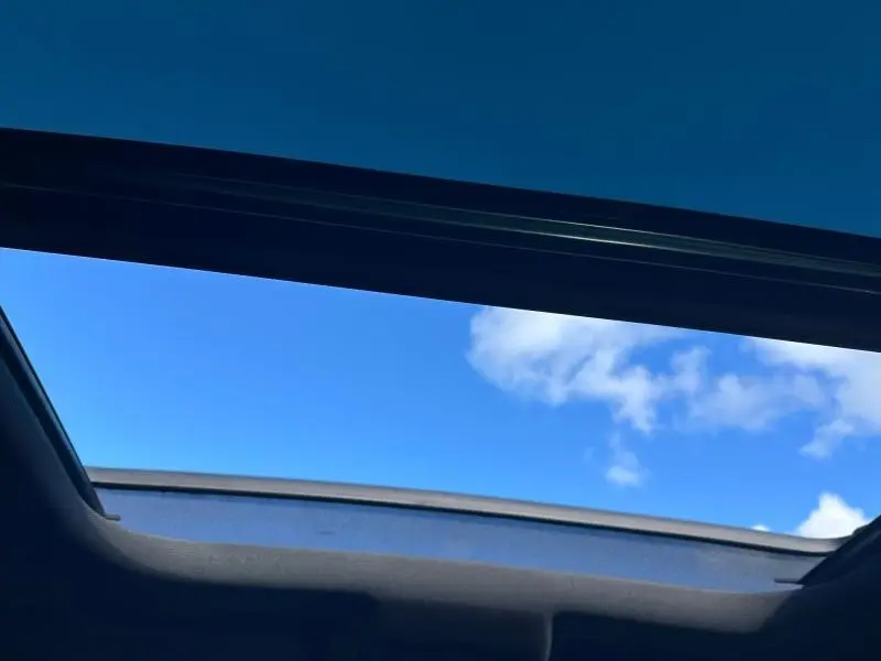 Vue intérieure du toit ouvrant panoramique de la Peugeot 308 gris Artense, avec ciel bleu visible à travers l'ouverture.