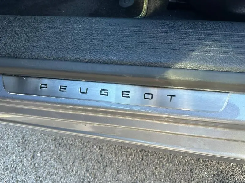 Gros plan sur la plaque de seuil de porte Peugeot en métal brossé, sur la carrosserie gris Artense.