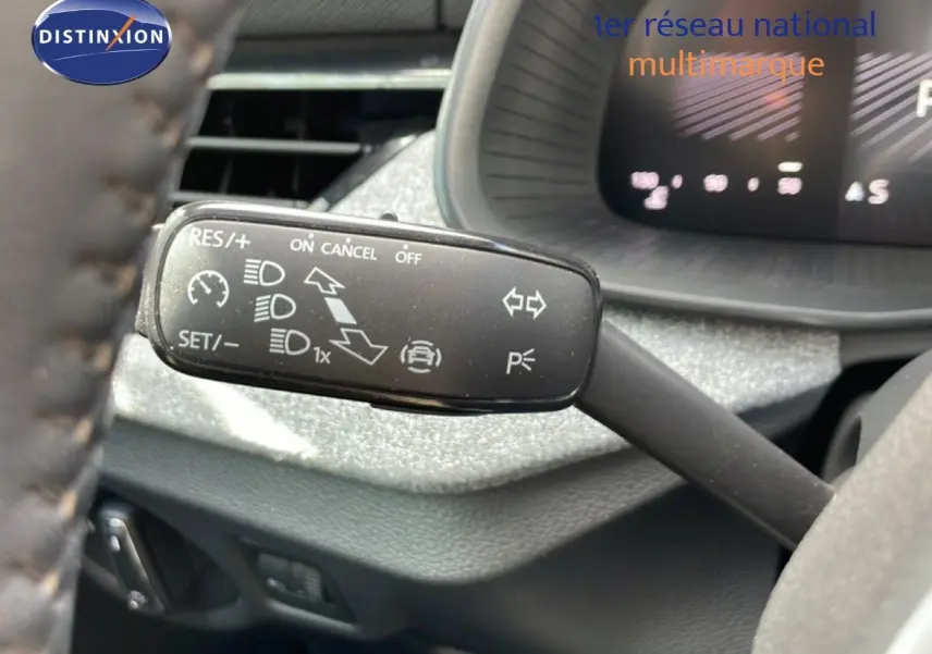 Gros plan sur la commande de régulateur de vitesse à gauche du volant dans l’habitacle gris noir d’une Skoda Scala blanche.