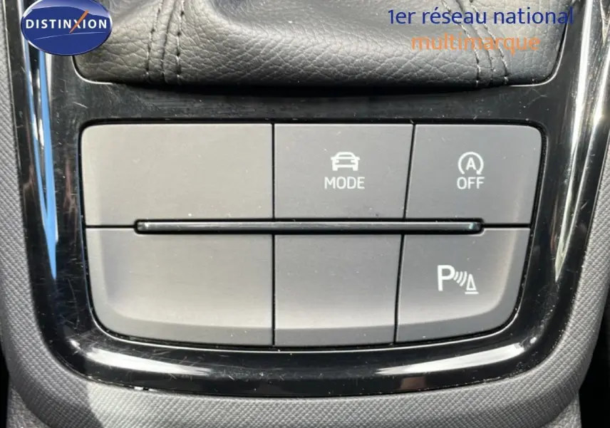 Gros plan sur les boutons de commande du mode de conduite et de l’aide au stationnement dans une Skoda Scala blanche Glacier 2025.