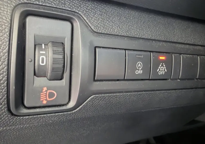 Gros plan sur les commandes noires du tableau de bord de la Peugeot 308 gris foncé, avec témoin lumineux rouge allumé.
