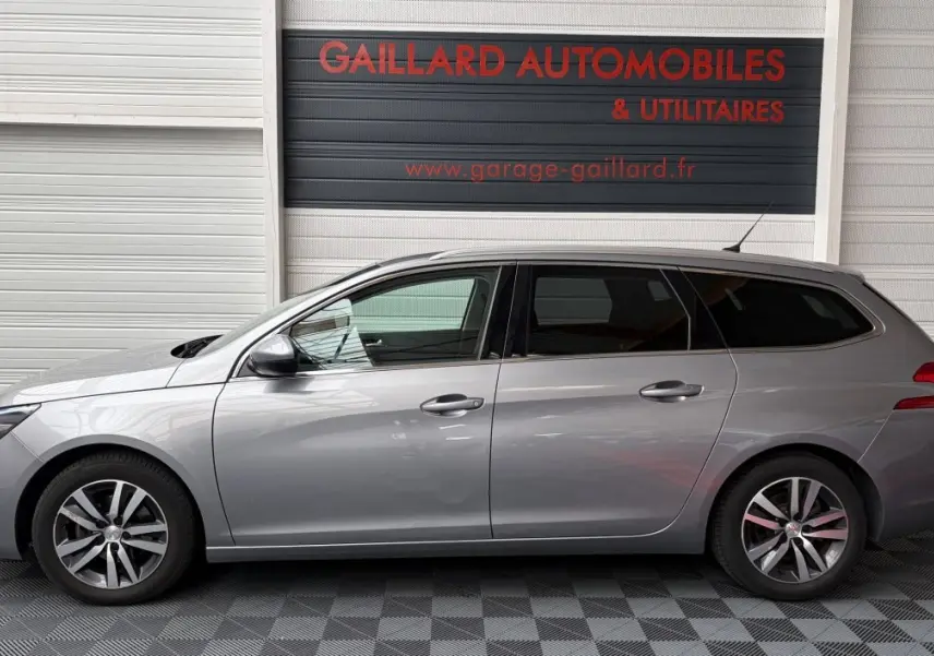 Profil côté gauche d'une Peugeot 308 SW gris foncé, vue en intérieur de garage avec jantes alliage et vitres teintées.
