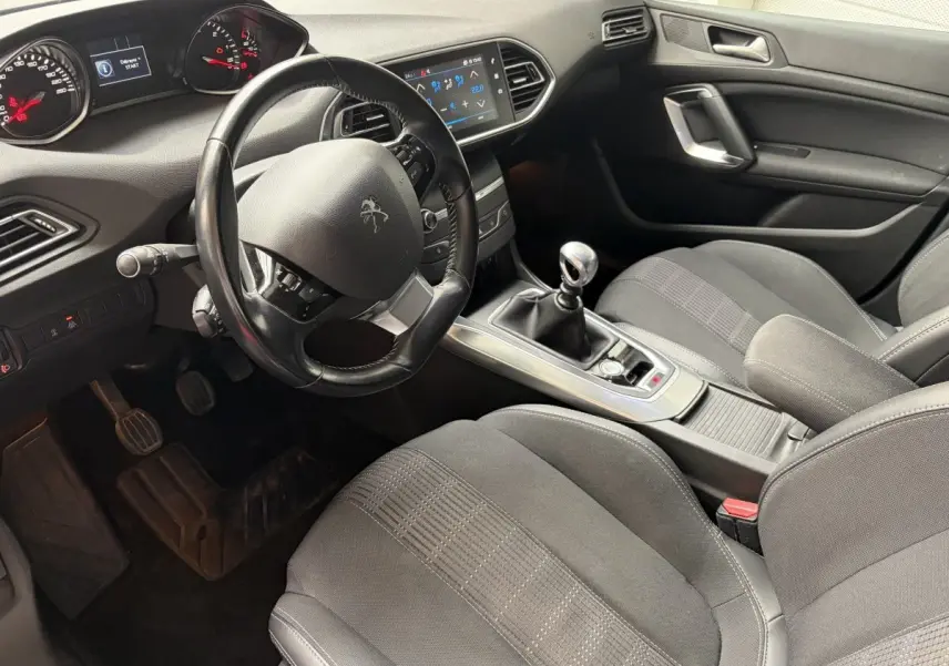 Vue intérieure côté conducteur de la Peugeot 308 gris foncé, volant cuir multifonctions et écran tactile central visible.