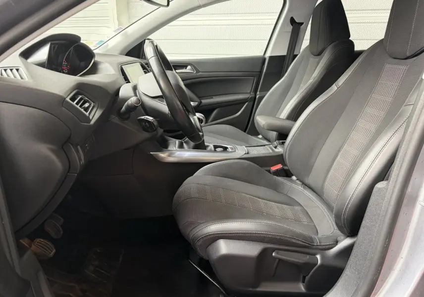 Vue intérieure côté conducteur de la Peugeot 308 gris foncé, montrant sièges tissu et volant cuir multifonctions.