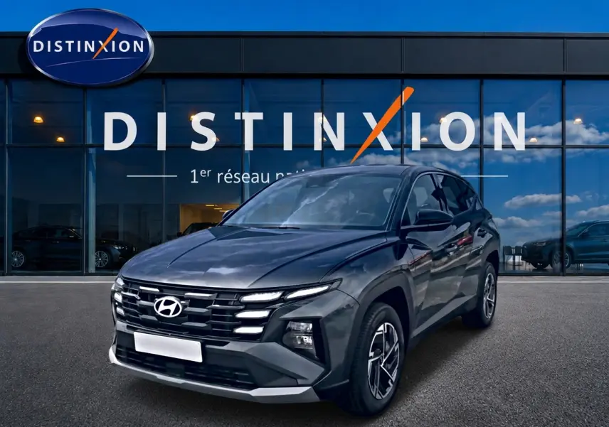 Hyundai Tucson 1.6 t-gdi 239 hybride gris ecotronique en 3/4 avant droit devant une vitrine Distinxion.