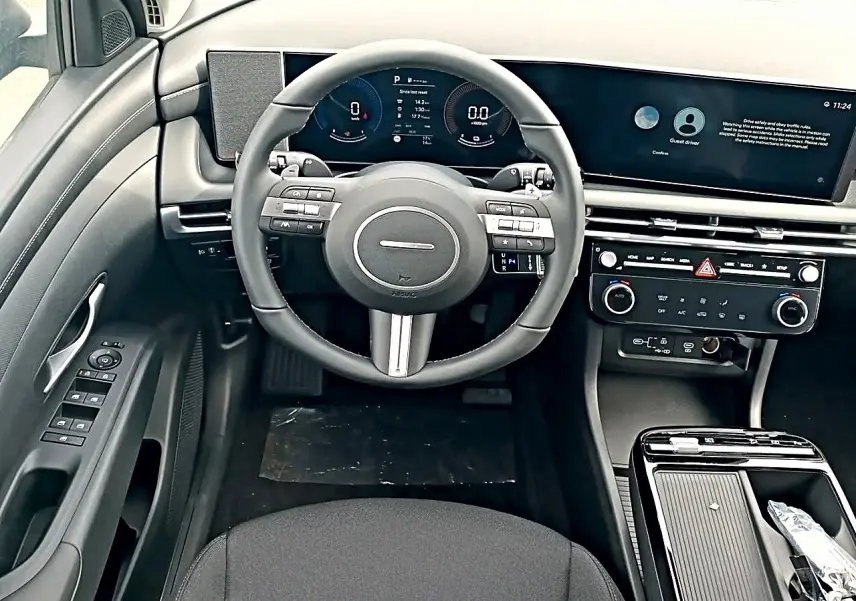 Vue intérieure frontale du tableau de bord et volant cuir multifonctions du Hyundai Tucson 2026, finition hybride, avec écran large numérique.