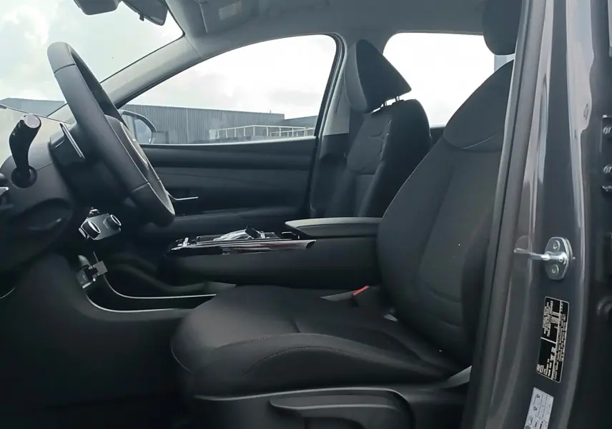 Vue intérieure côté conducteur du Hyundai Tucson gris ecotronique, montrant les sièges noirs et l'accoudoir central.