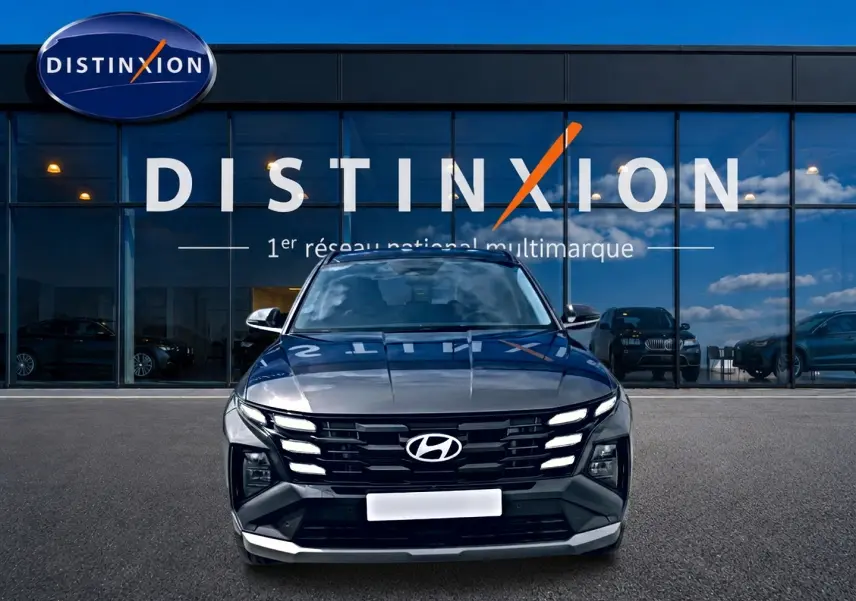Vue frontale d’un Hyundai Tucson gris ecotronique avec calandre noire et feux LED allumés devant un showroom Distinxion.