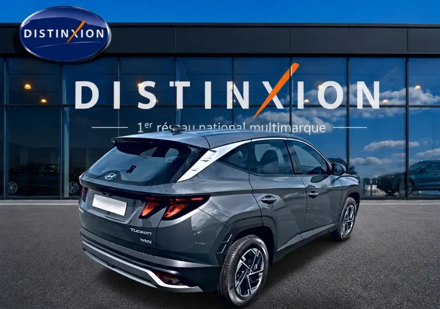 Vue 3/4 arrière droite du Hyundai Tucson gris ecotronique avec jantes alliage et vitres teintées devant un showroom Distinxion.