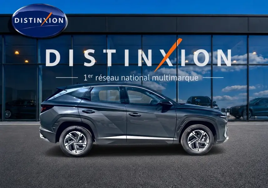 Hyundai Tucson 2026 gris ecotronique vu de profil côté gauche devant une vitrine Distinxion.
