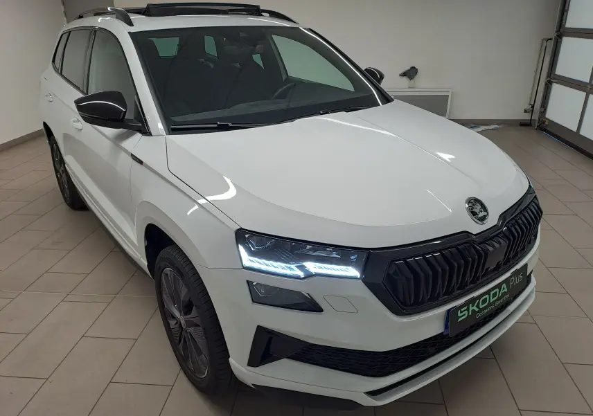 Vue 3/4 avant droit du Skoda Karoq blanc Lune avec phares LED allumés et calandre noire sportive.