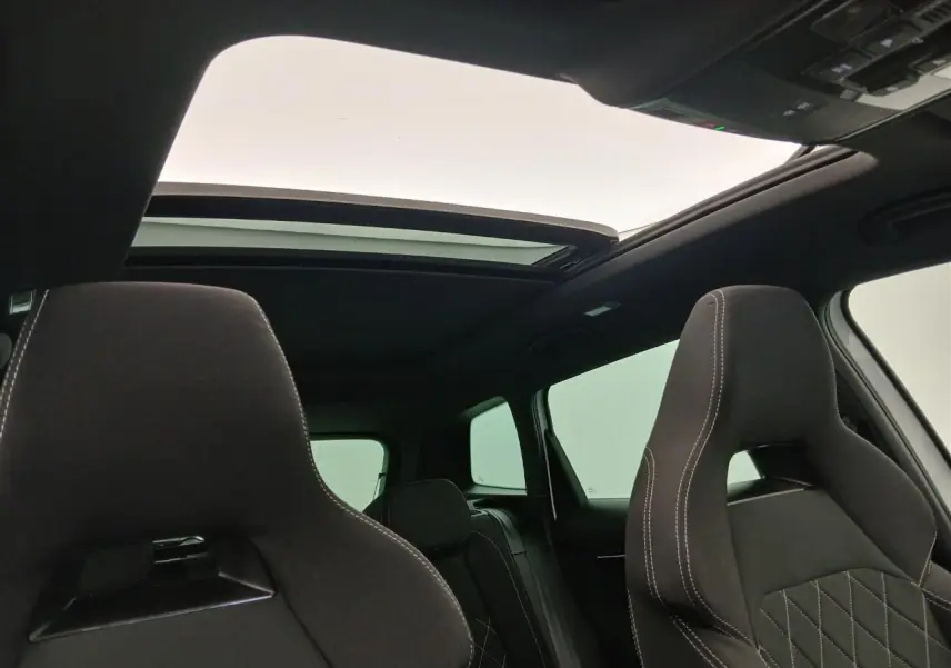 Vue intérieure du toit ouvrant panoramique en verre et des sièges avant noirs avec surpiqûres blanches du Skoda Karoq Blanc Lune.