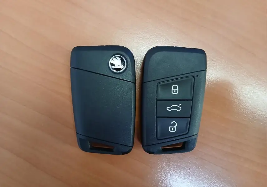 Deux clés noires de voiture Skoda posées sur une surface en bois, vues de face et de dos.