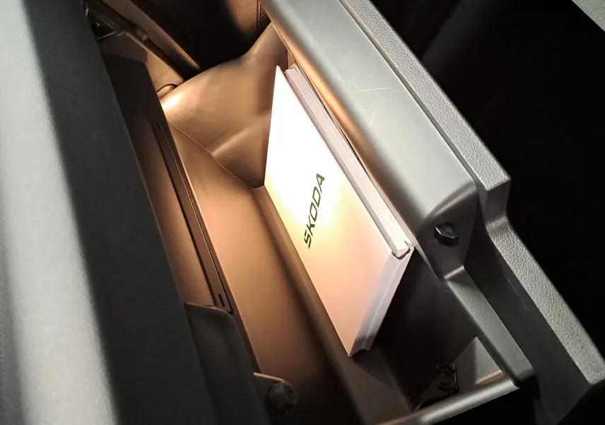 Vue rapprochée de la boîte à gants ouverte du Skoda Karoq 2025 avec manuel et éclairage intérieur.