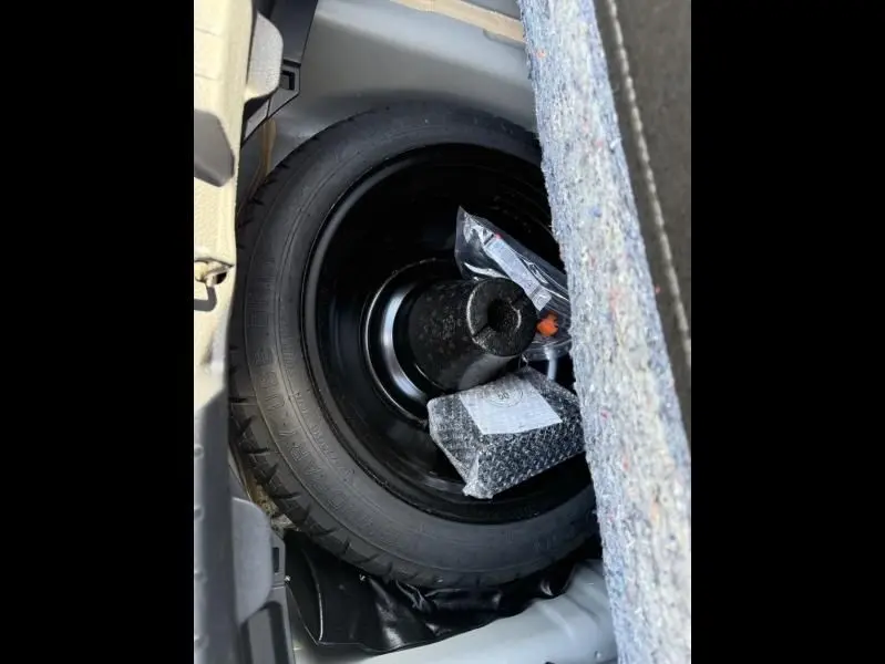 Roue de secours noire dans le coffre d'une Toyota Yaris gris métal 2020, avec outils de changement rangés dessus.