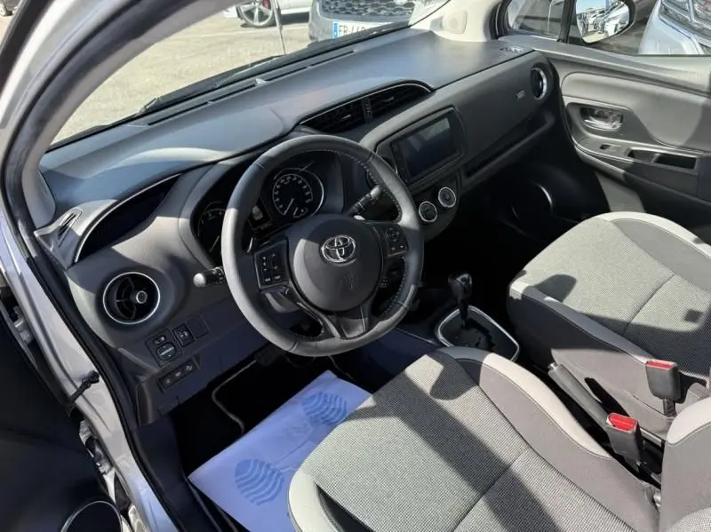 Vue intérieure côté conducteur de la Toyota Yaris 2020 gris métal, avec tableau de bord et volant multifonction visibles.