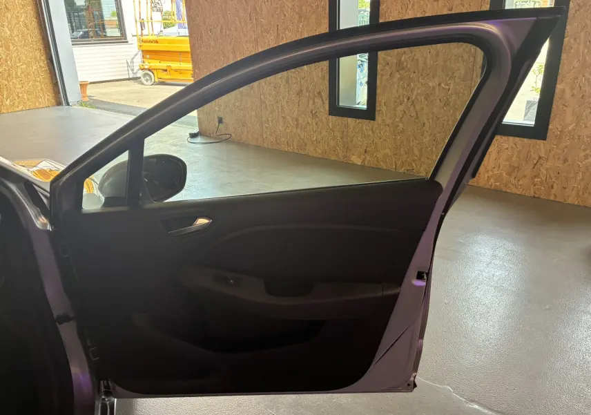 Vue intérieure de la porte avant gauche ouverte d'une Renault Clio gris 2022, avec panneau noir et poignée intégrée.