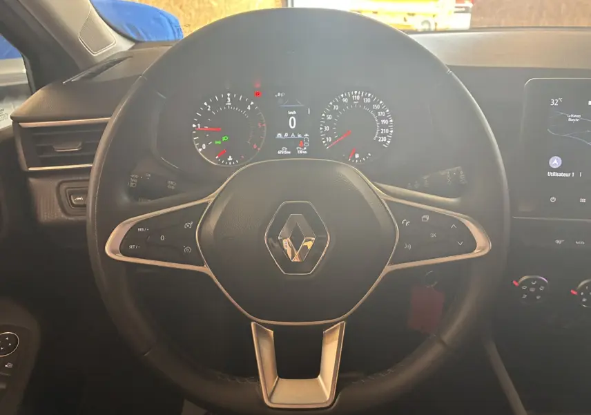 Vue rapprochée du volant noir de la Renault Clio 1.5 BlueDCI Business 2022 avec tableau de bord et commandes visibles.