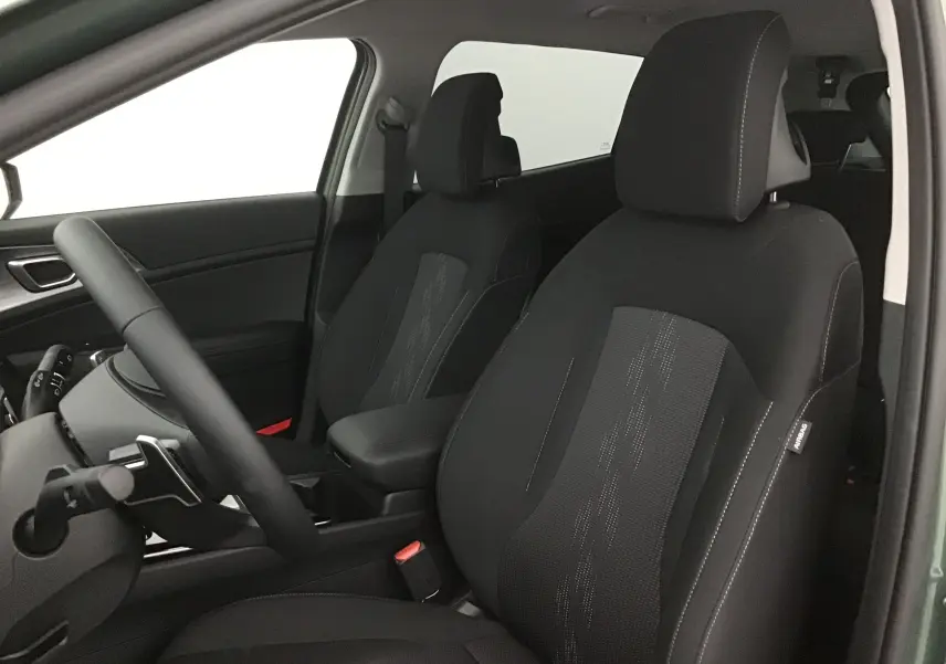 Vue intérieure côté conducteur du Kia Sportage 2025, sièges noirs avec surpiqûres blanches et accoudoir central.