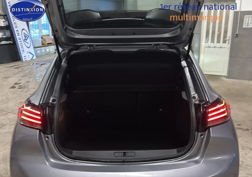 Vue arrière d'une Peugeot 208 gris artense avec coffre ouvert et feux arrière LED allumés dans un garage.