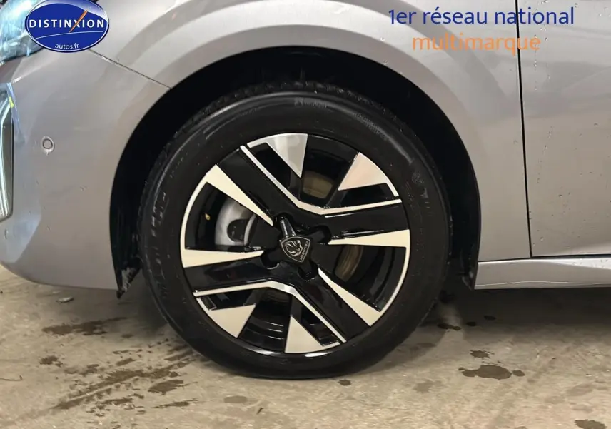 Gros plan sur la roue avant gauche avec jante alu bicolore du Peugeot 208 gris Artense 2025.