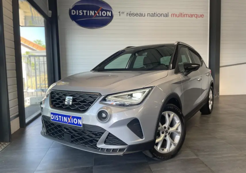 Vue 3/4 avant droite d'une SEAT Arona 2024 gris clair GRS avec jantes alliage et calandre noire en showroom.