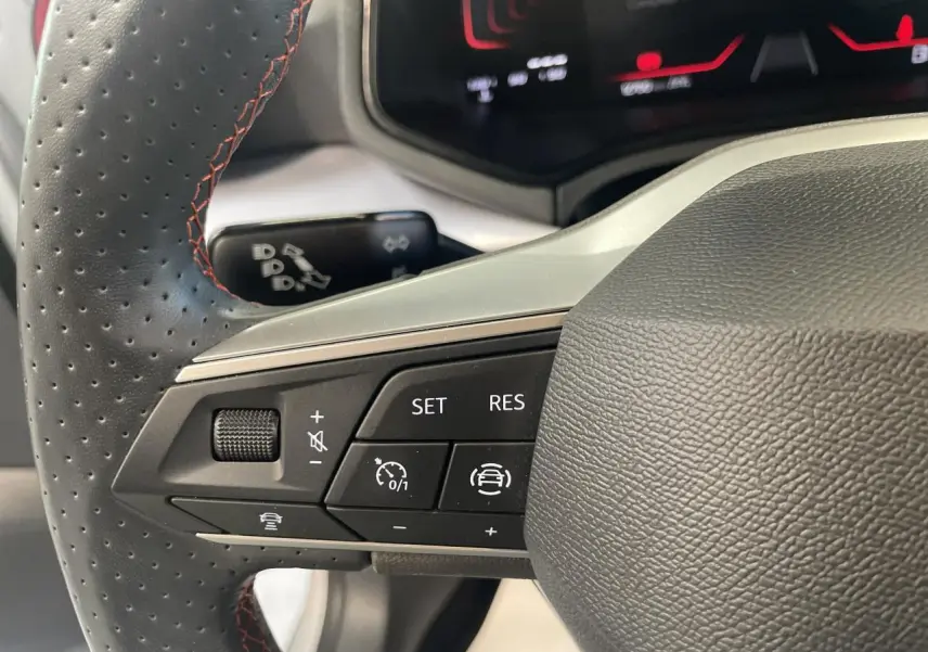 Gros plan sur le volant cuir noir perforé avec surpiqûres rouges du SEAT Arona 2024, boutons de régulateur de vitesse visibles.