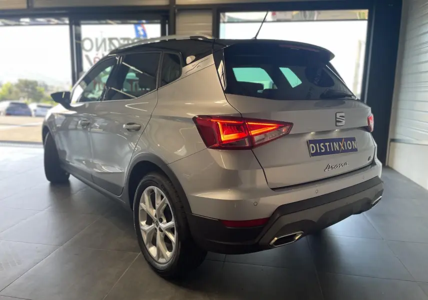 Vue 3/4 arrière droite d'une SEAT Arona 2024 rouge passion avec feux arrière allumés en showroom.