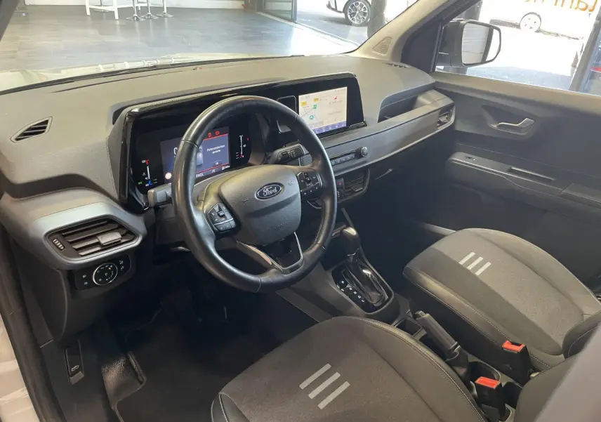Vue intérieure avant du Ford Tourneo Courier 2024, volant cuir noir, écran tactile 8 pouces et sièges tissu gris foncé.