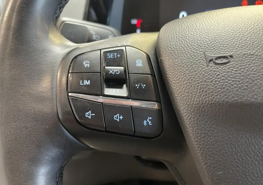 Gros plan sur les commandes multifonctions noires à gauche du volant cuir synthétique du Ford Tourneo Courier gris clair.