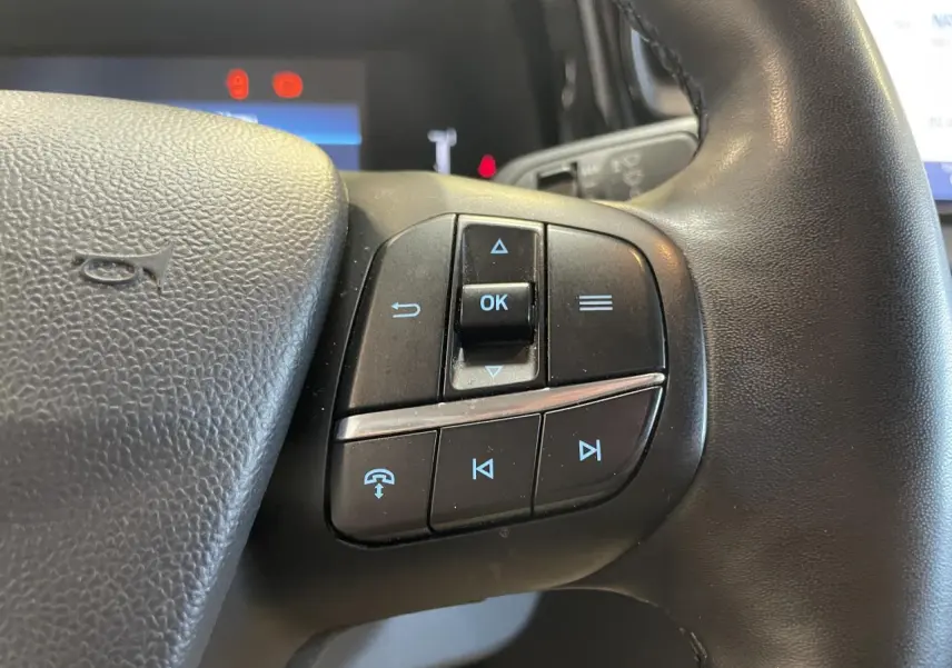Gros plan sur les commandes multifonctions noires du volant cuir synthétique du Ford Tourneo Courier 2024.