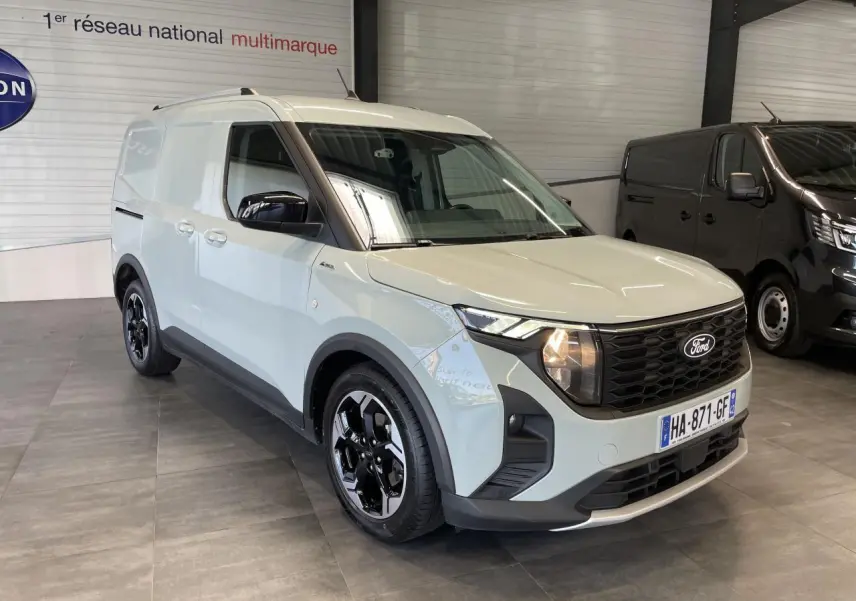 Ford Tourneo Courier gris clair en 3/4 avant droit, avec calandre noire nid d'abeille et jantes alu noires.