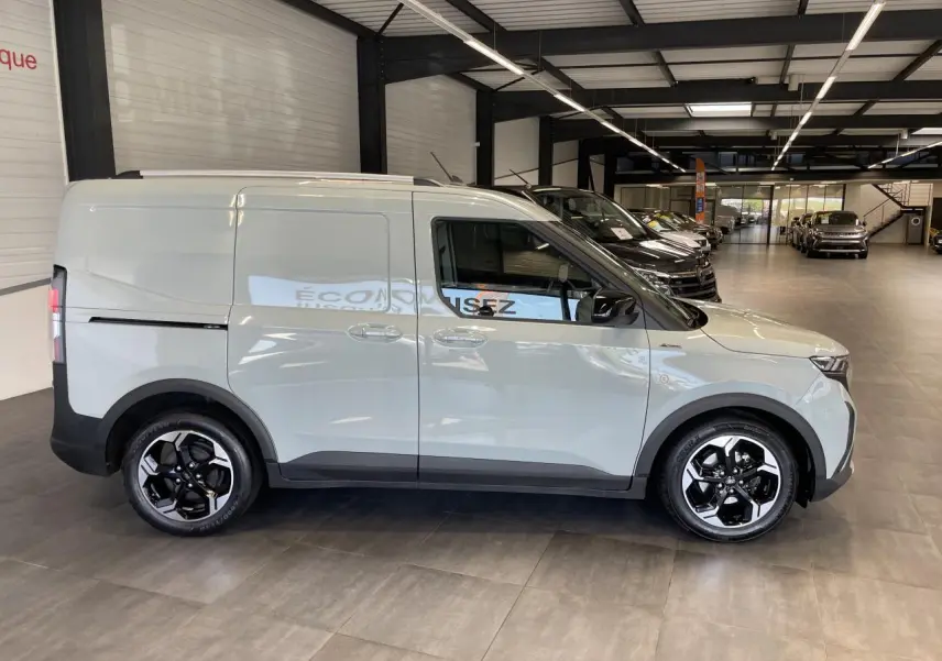Ford Tourneo Courier gris clair vu de profil côté gauche, avec jantes alliage noires et toit équipé de barres.