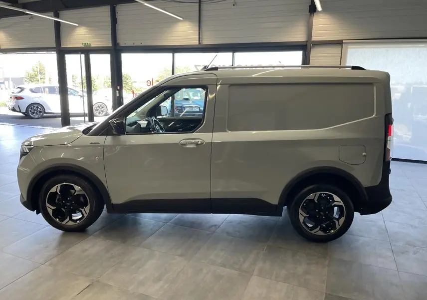 Vue de profil côté gauche du Ford Tourneo Courier 2024 gris clair avec jantes aluminium noires et toit noir.