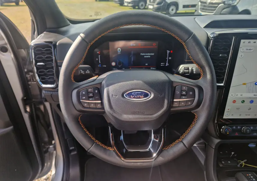 Gros plan sur les commandes au volant du Ford Ranger Super Cabine gris Iconic, avec surpiqûres orange visibles.
