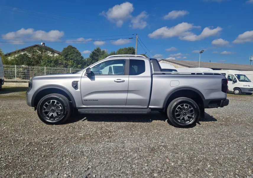 Ford Ranger Wildtrak gris iconic vu de profil côté gauche sur un sol gravillonné avec benne protégée.