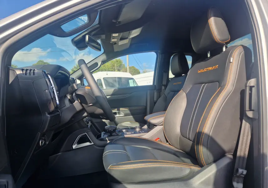 Vue intérieure arrière du Ford Ranger Super Cabine 2025, sièges noirs avec surpiqûres orange et vitre arrière donnant sur la benne.