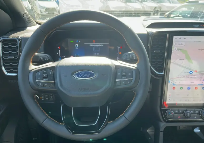 Vue intérieure centrée sur le volant du Ford Ranger 2.3 PHEV 281 Wildtrak Plus 2025 avec écran tactile et finition noire.