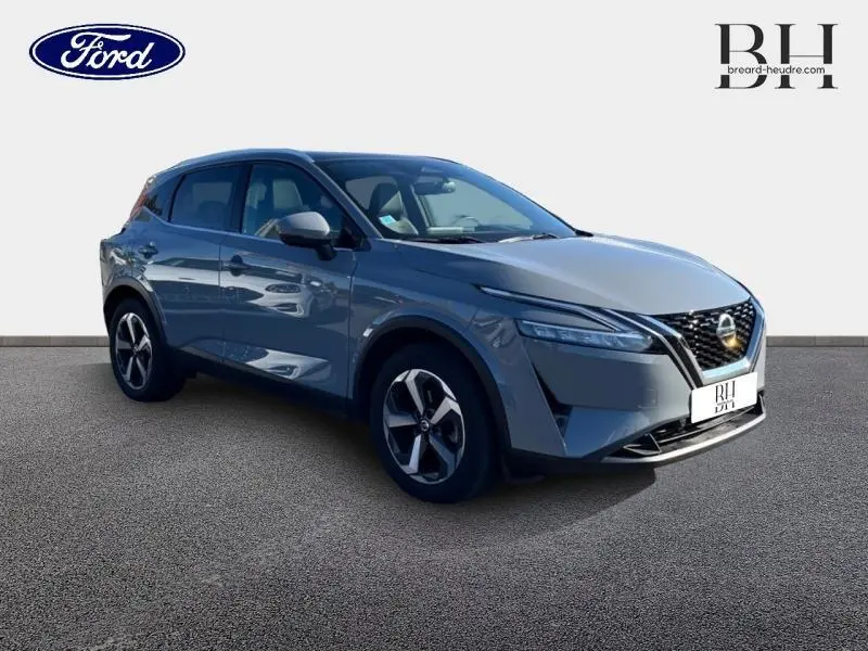 Nissan Qashqai gris argile en 3/4 avant droit, avec calandre noire et jantes alliage distinctives.