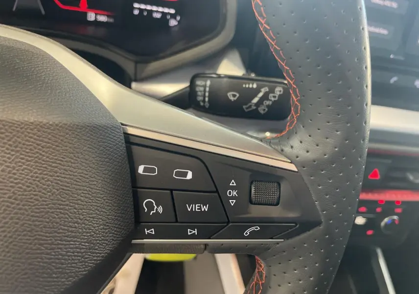 Gros plan sur le volant cuir perforé noir avec surpiqûres rouges du SEAT Arona 2024, boutons multifonctions visibles.