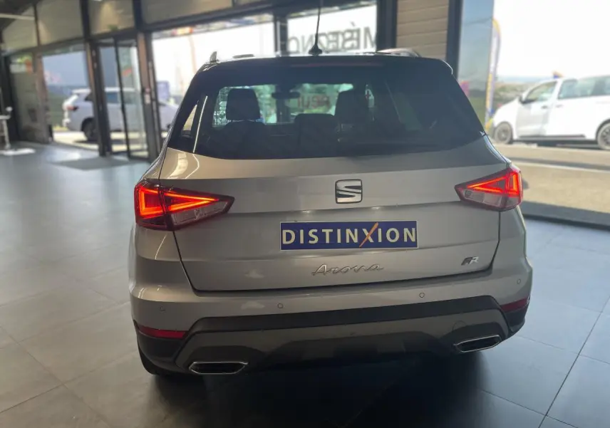 Vue arrière d'un SEAT Arona 2024 gris GRS avec feux allumés et badge FR, en intérieur de showroom.