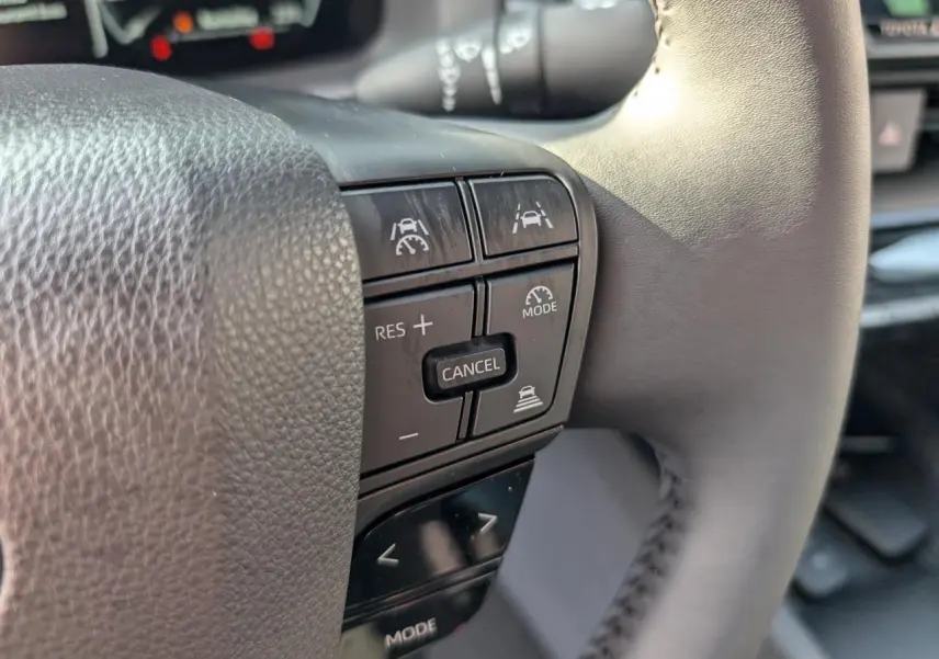 Gros plan sur le volant côté gauche du Toyota C-HR blanc 2024, avec commandes de régulateur et aide à la conduite.